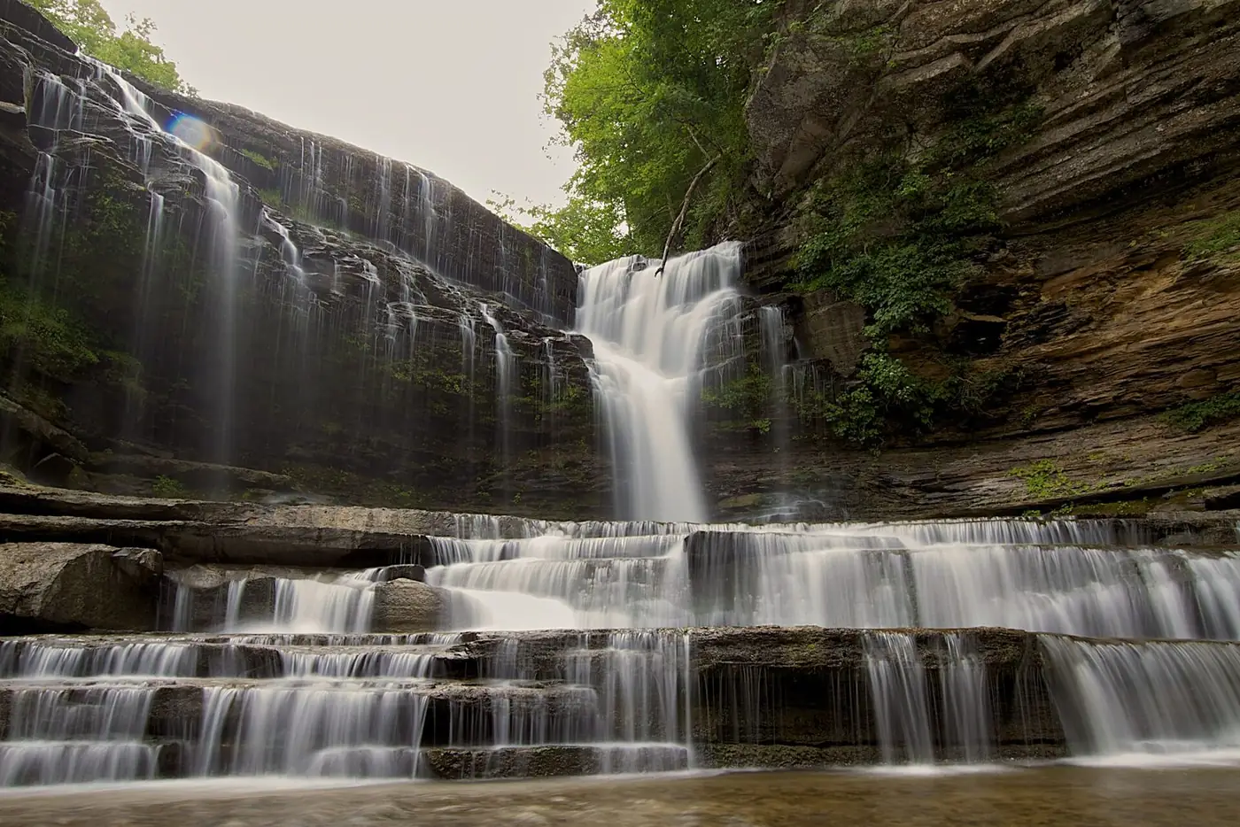 Cummins Falls spilling over layered limestone ledges into a pool, with woods above
